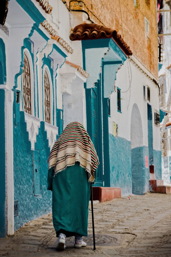 Crafting Captivating Headlines: Your awesome post title goes here Elderly woman with shawl and cane walking along vibrant blue city street.