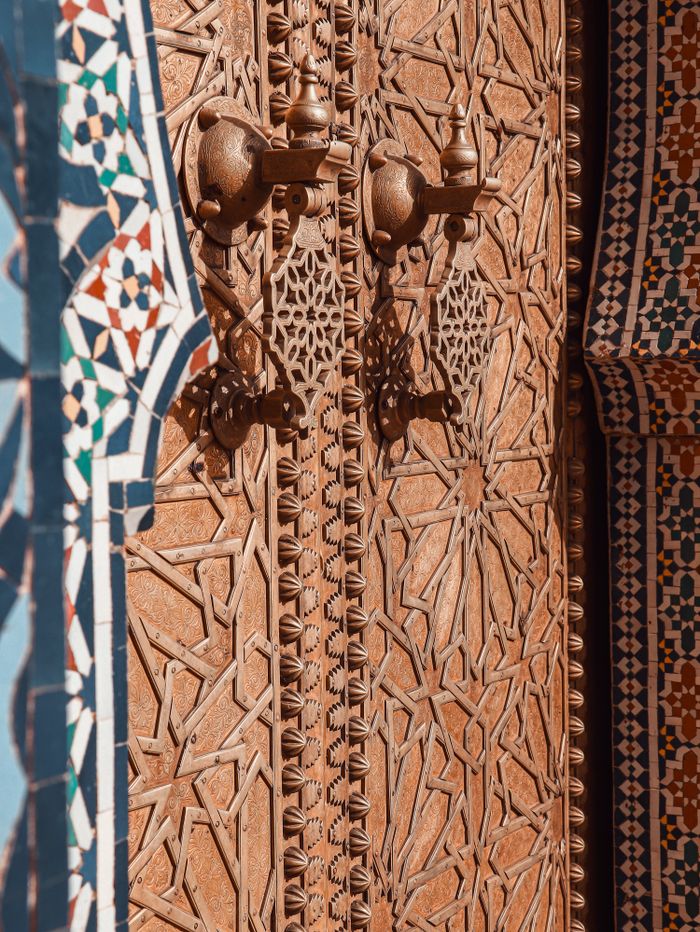 portfolio-02 Close-up of a beautifully crafted Moroccan door featuring traditional intricate patterns and copper details.