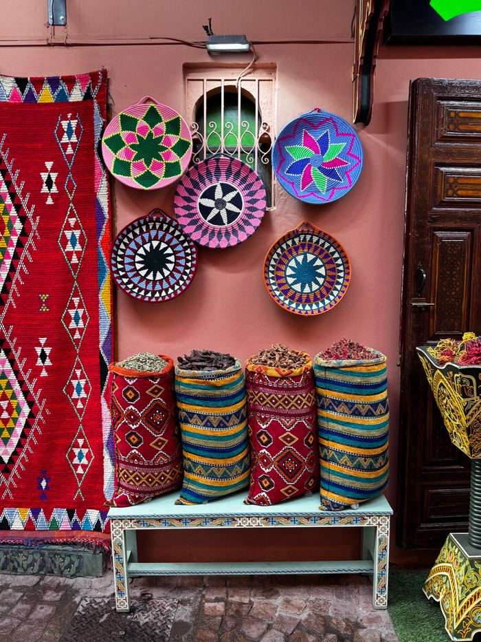 portfolio-08 Vibrant market display in Marrakech showcasing colorful textiles and baskets with spices.