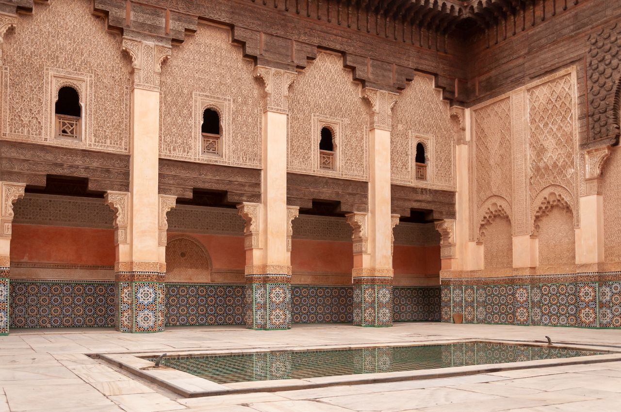 portfolio-07 Main courtyard of ancient Ben Youssef Madrasa with arched passage and walls decorated with arabesque ornaments on sunny day in Marrakesh